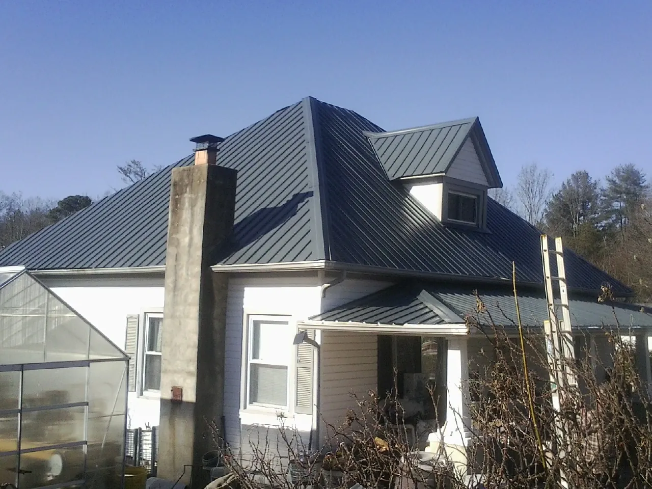 Dark blue standing seam metal roof on a white farmhouse with dormer — Slate & Tile Roof Repair by Roofing Brothers in Arbovale