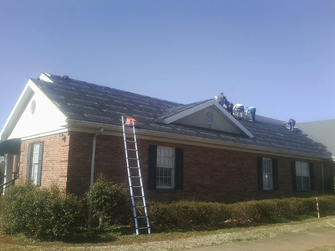 Crew tearing shingles off a brick ranch roof with a ladder set — Emergency Roof Repair work by our crew in Arbovale