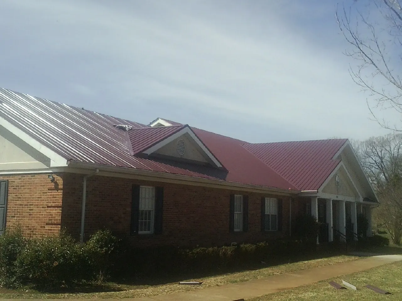 Red metal roof with gabled entries on a long brick building, from a Hail Damage Roof Repair job in Arbovale