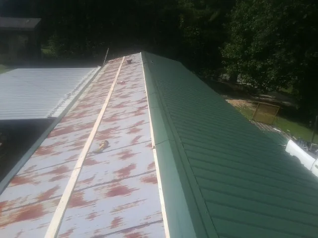 Old rusted panels beside newly installed green metal roofing — Wind Damage Roof Repair by Roofing Brothers in Arbovale
