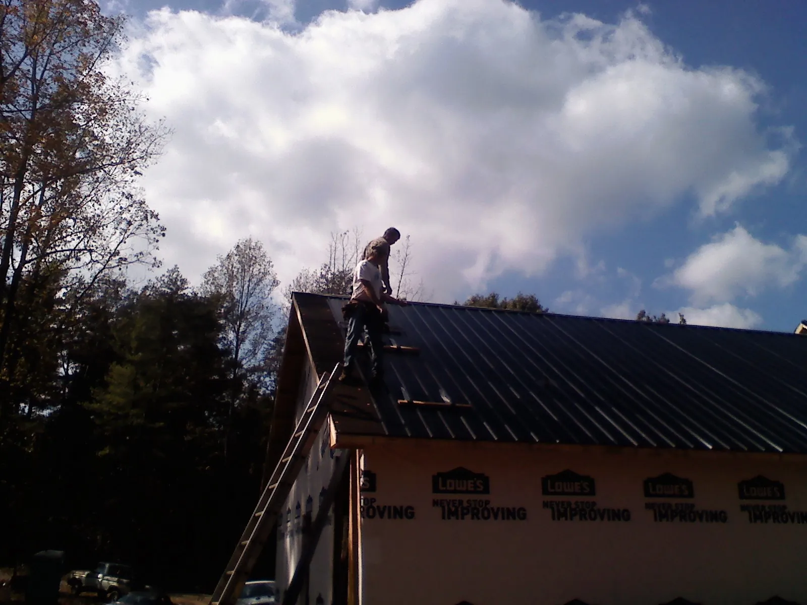 Roofer fastening dark metal panels high against a cloudy sky, from a Roof Inspection job in Arbovale