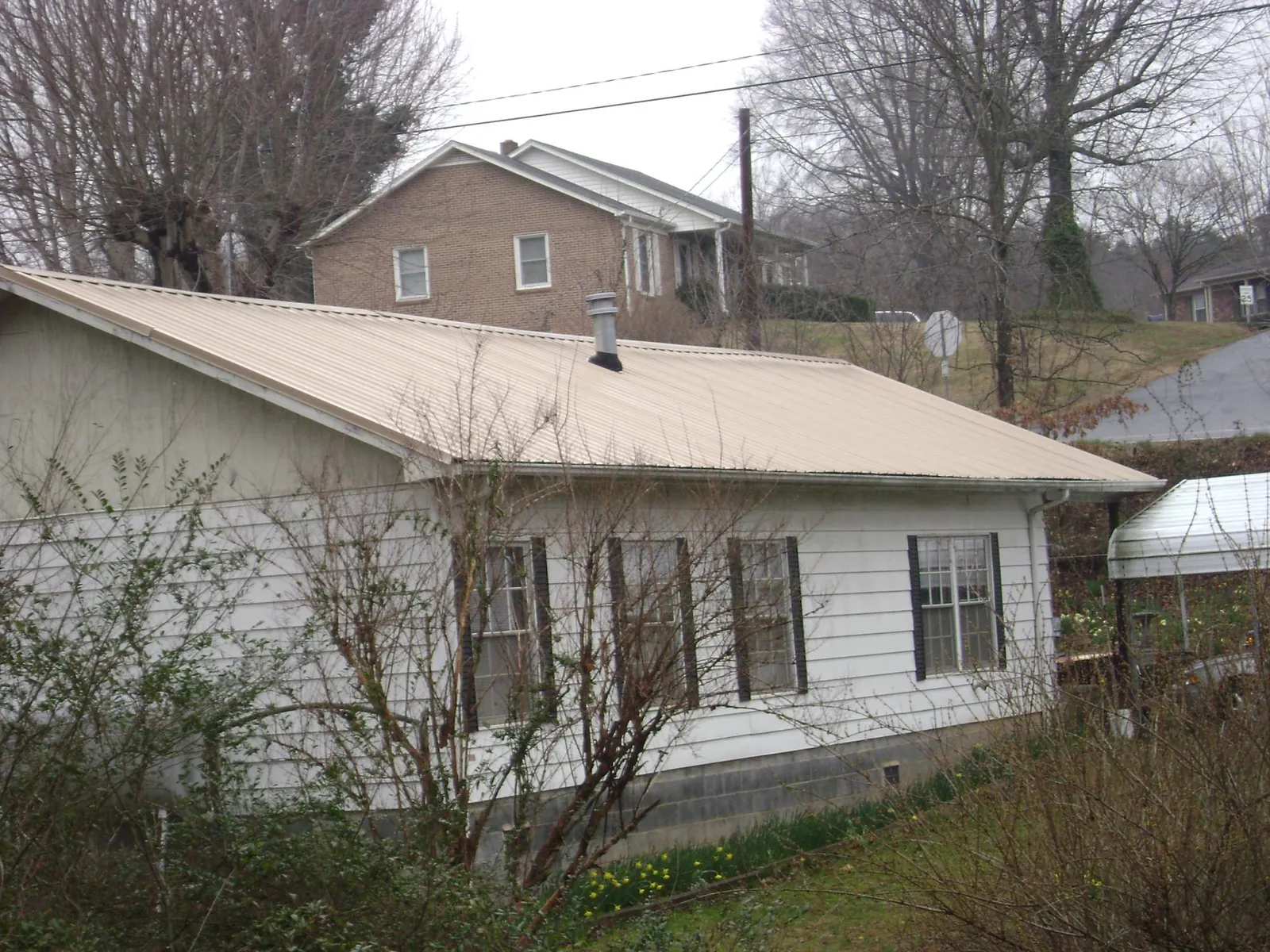 Tan metal roof on a white sided house set into a hillside — Commercial Roofing by Roofing Brothers in Arbovale